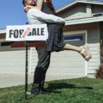 Happy couple hugging in front of their newly purchased home with a "Sold" sign